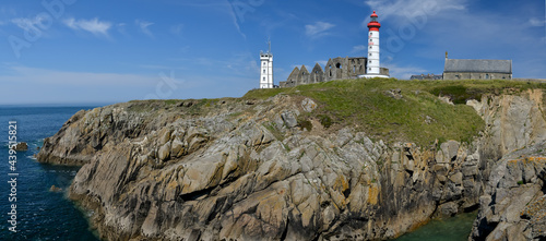 panoramique sur falaise de granit avec le phare blanc et rouge de la pointe Saint Mathieu et son Abbaye du Finistère en ruine sous un ciel bleu de Bretagne 