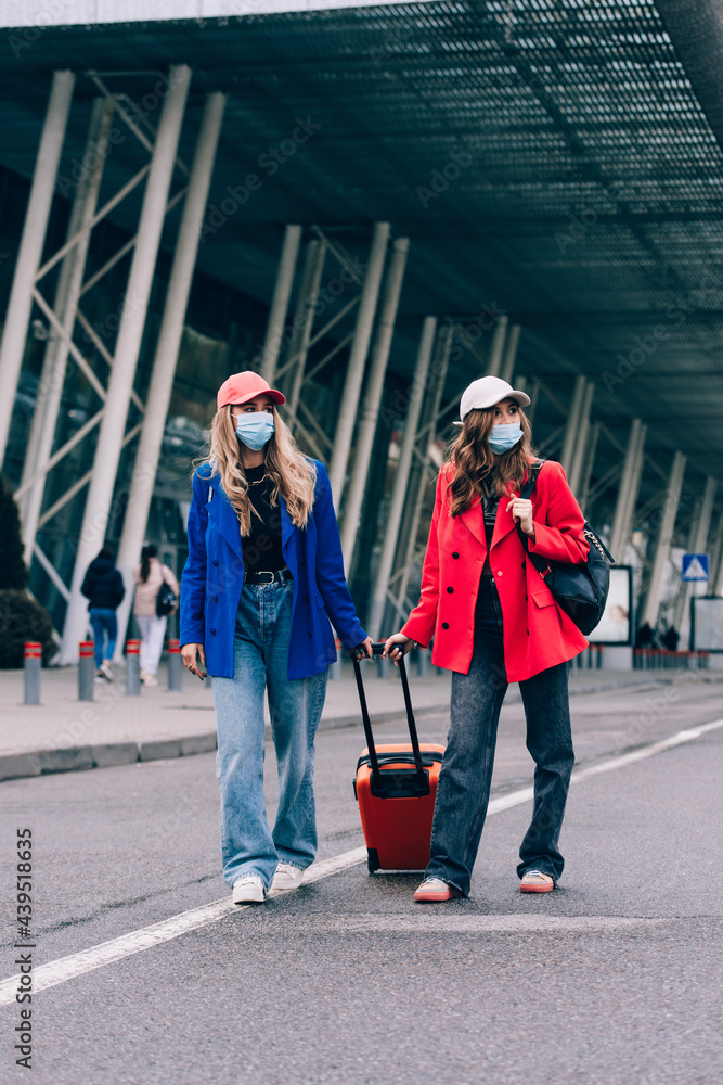 Obraz premium Two happy girls walking near airport, with luggage. Air travel, summer holiday