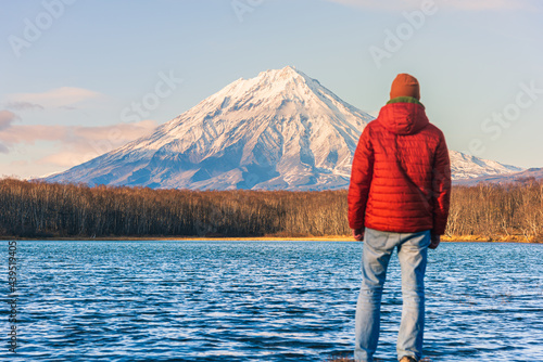A man dressed in red looks at a majestic volcano on Russia's famed Kamchatka Peninsula. Inspiring pictures of travel.