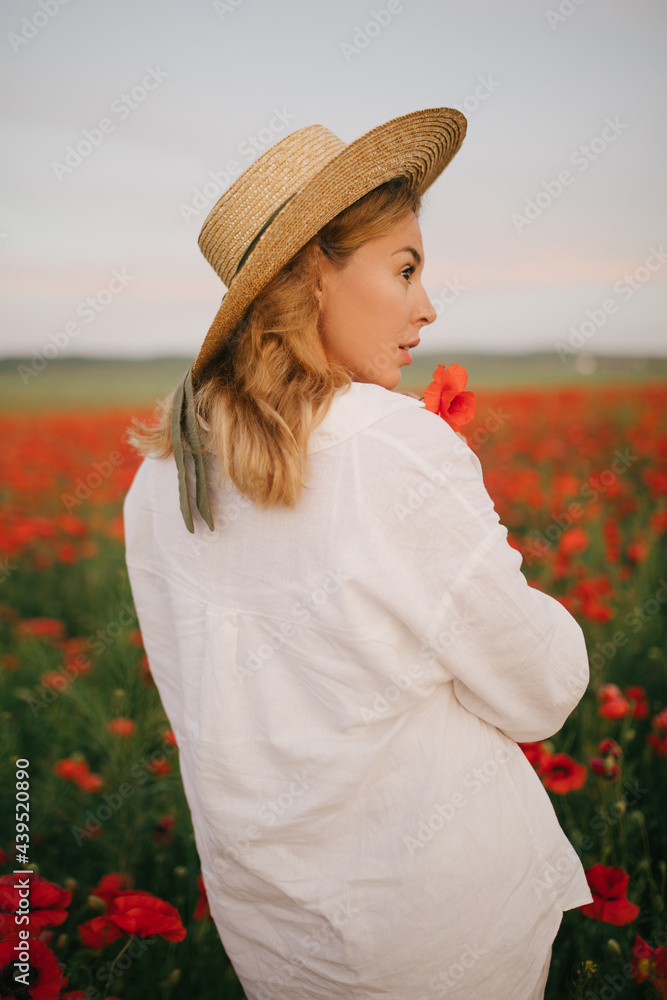 Young beautiful woman wearing white linen suit and straw hat posing in a poppy field.