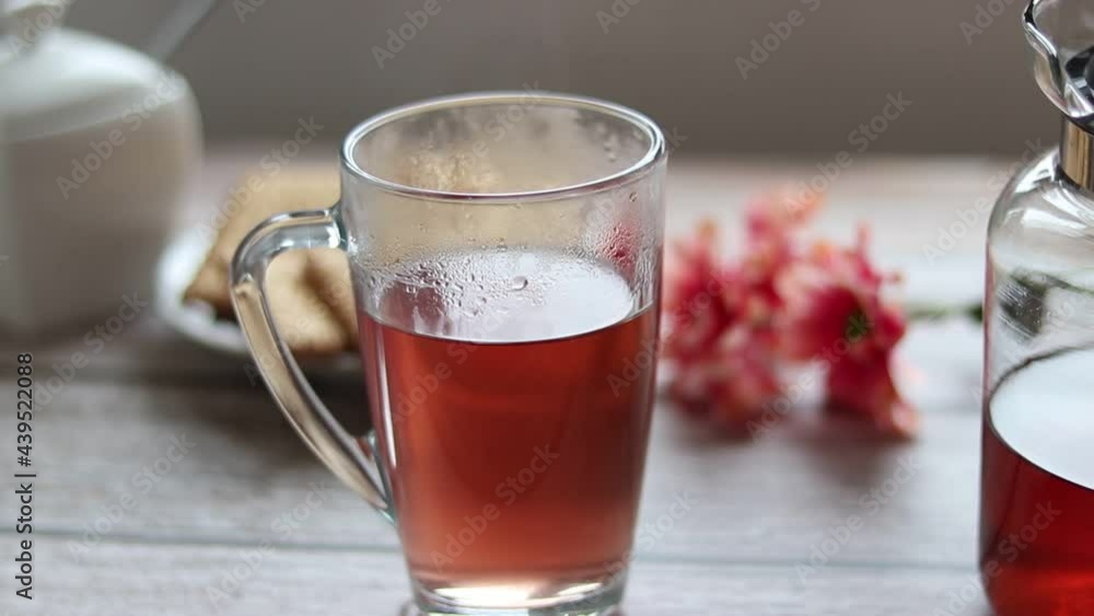 Pouring fruit tea into a transparent cup. In the background are cookies and a sugar bowl. Pouring fruit tea into a transparent cup. In the background are cookies and a sugar bowl.