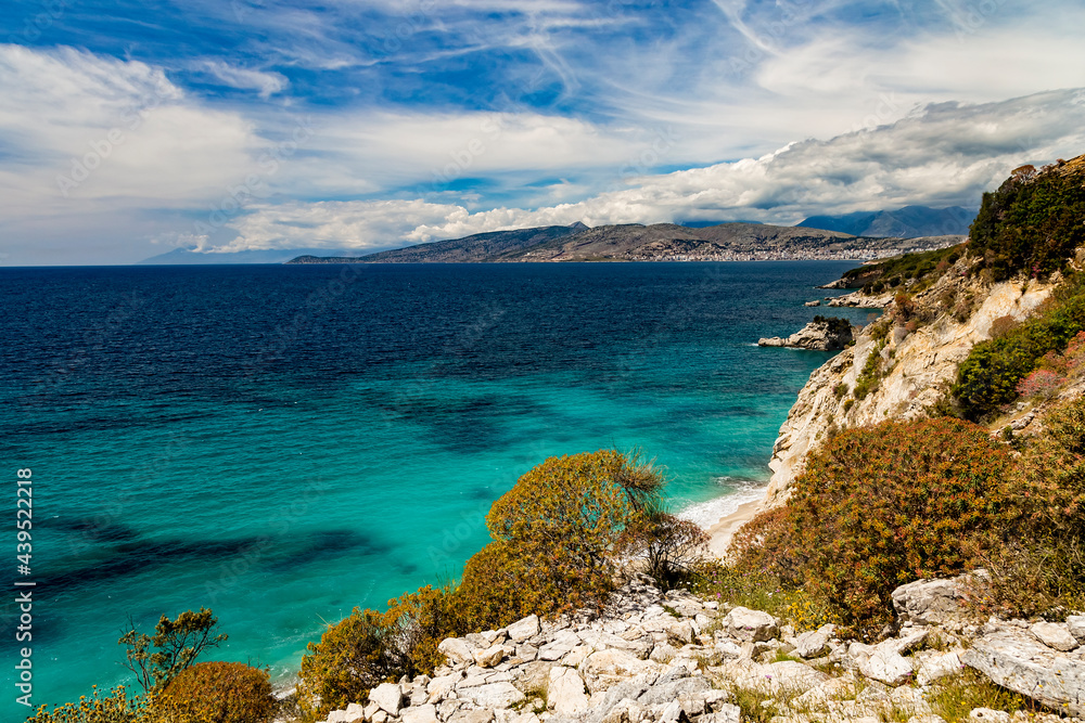 Albania, Saranda resort. View of the rocks, beach and the sea, Corfu island is on the horisont. Blue sea and sky with white clouds. Ionian Sea.