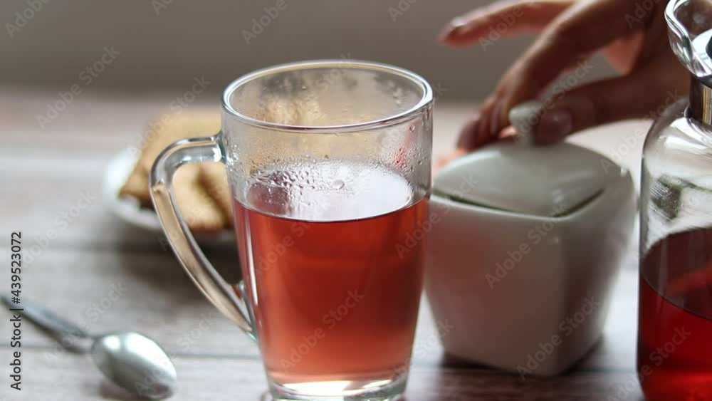 Pouring fruit tea into a transparent cup. In the background are cookies and a sugar bowl. Pouring fruit tea into a transparent cup. In the background are cookies and a sugar bowl.