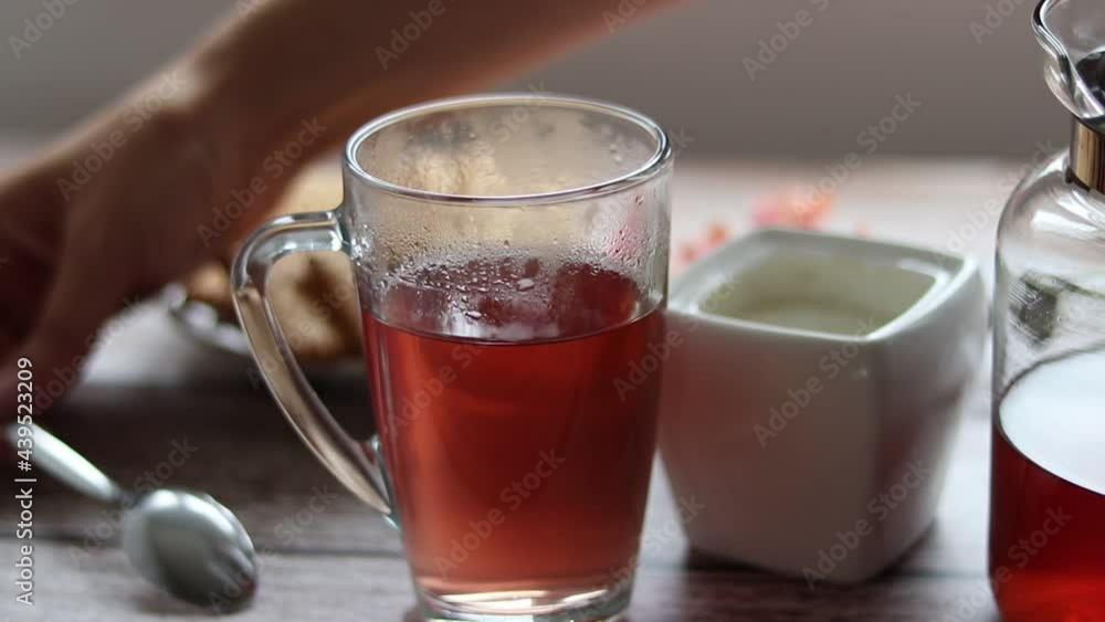 Pouring fruit tea into a transparent cup. In the background are cookies and a sugar bowl. Pouring fruit tea into a transparent cup. In the background are cookies and a sugar bowl.