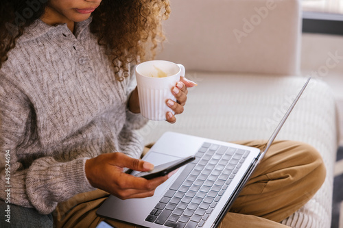 Young woman with cup of coffee using gadgets at home photo
