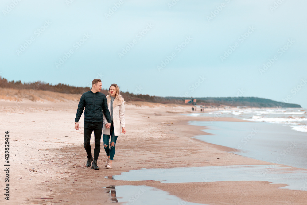 Attractive young couple walking along the shore of a sandy beach, on a spring romantic holiday, outdoors. Attractive young couple walking along the shore of a sandy beach, on a spring romantic holiday, outdoors.