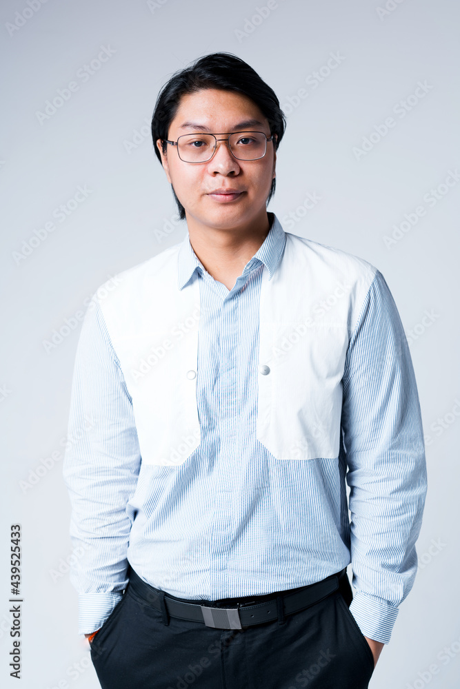 Handsome young asian businessman in shirt and glasses stands on white background with hands in pockets Handsome young asian businessman in shirt and glasses stands on white background with hands in pockets