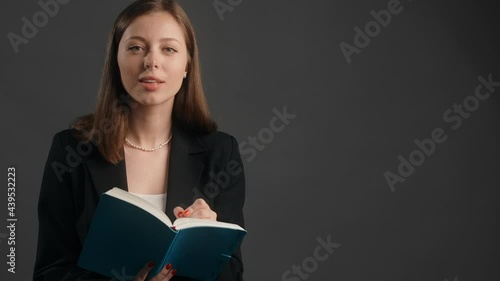 Young woman in black suit listens to the collocutor with smile and makes notes to the paper notepad, taking survey, making interview, 4k Prores HQ photo