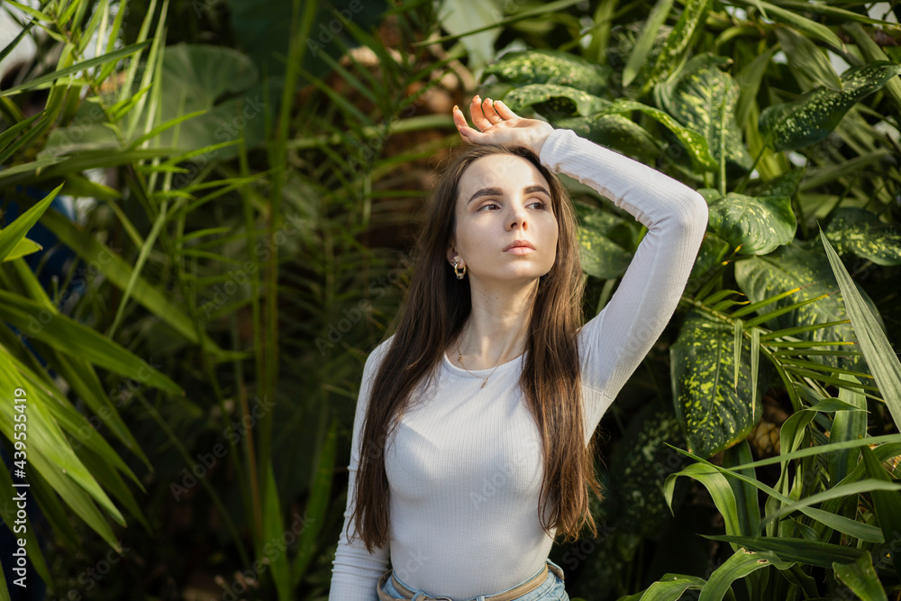a 25-year-old girl with long dark hair, European appearance, in a white T-shirt, standing by a tree with green leaves, with her hands up. Skin care, folk recipes, herbal treatments, healing, lonelines a 25-year-old girl with long dark hair, European appearance, in a white T-shirt, standing by a tree with green leaves, with her hands up. Skin care, folk recipes, herbal treatments, healing, lonelines