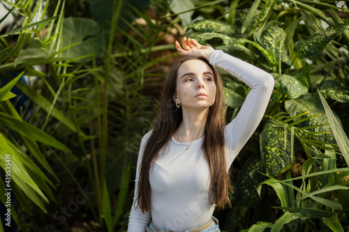 a 25-year-old girl with long dark hair  European appearance  in a white T-shirt  standing by a tree with green leaves  with her hands up. Skin care  folk recipes  herbal treatments  healing  lonelines