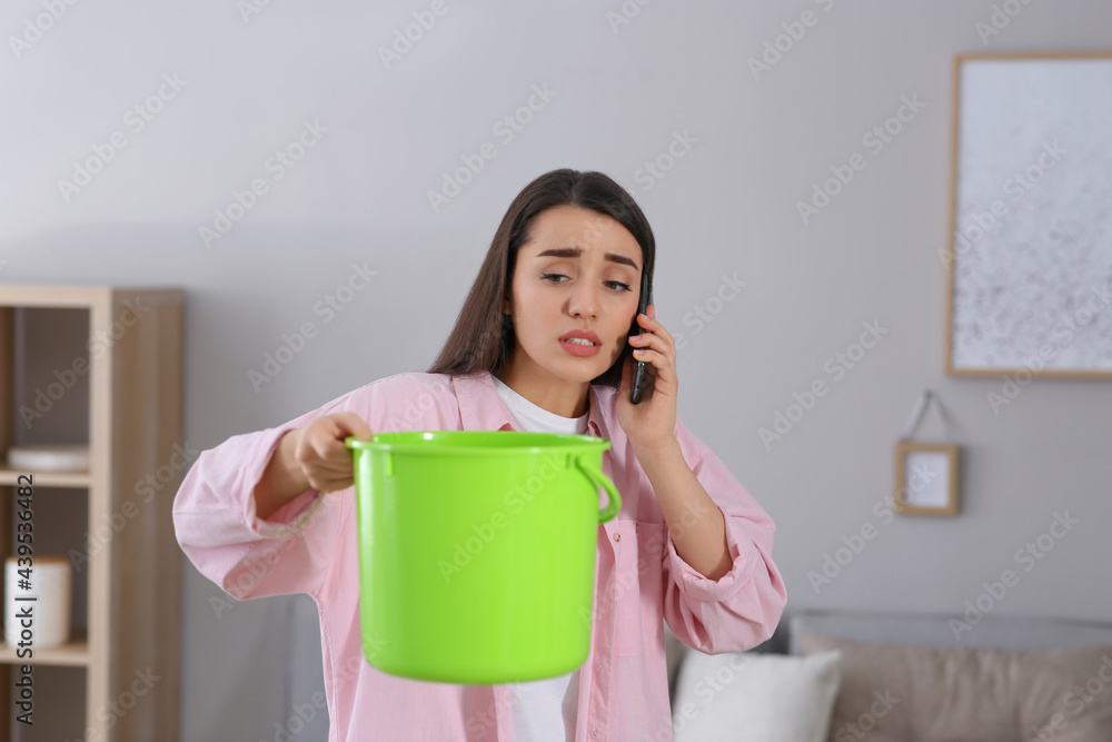 Young woman calling roof repair service while collecting leaking water from ceiling at home Young woman calling roof repair service while collecting leaking water from ceiling at home