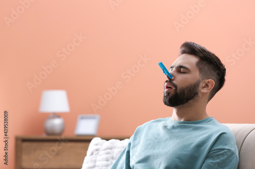 Man with clothespin suffering from runny nose at home. Space for text photo