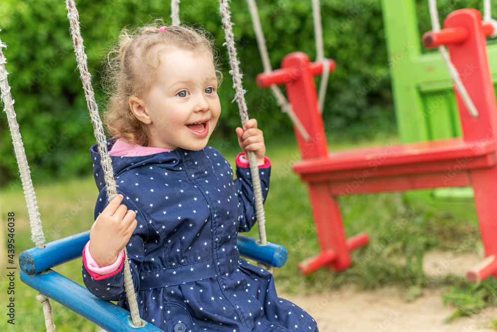 Little joyful girl swinging on a swing.