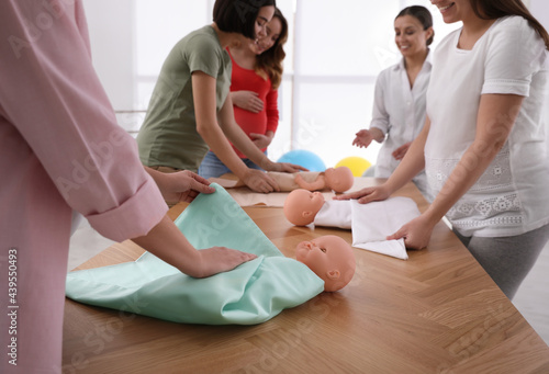 Pregnant women learning how to swaddle baby at courses for expectant mothers indoors, closeup