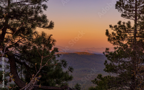 In Payson  Arizona this is known as the Mogollon Rim. The sun sets looking out over the rim  through the trees  the colorful sky paints the ledge and flowing hills  boulders and trees colorful shades 