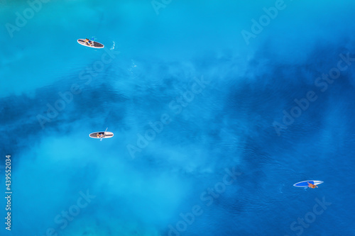 Aerial view of people on floating sup boards on blue sea at sunset in summer. Blue lagoon, Oludeniz, Turkey. Tropical landscape. Kayaks on clear water. Active travel. Top view of canoe. Sport