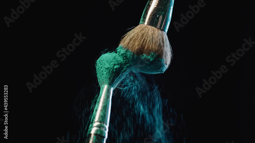cosmetic brushes hitting and making splashes of blue holi paint on black background