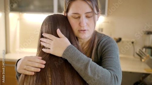 Young mother kissing and hugging upset crying daughter after talking about problems. Parent supporting and comforting child