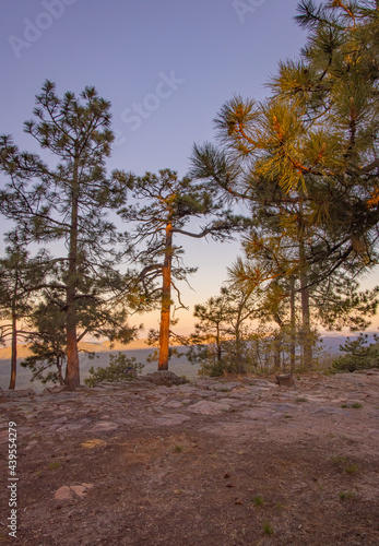 In Payson, Arizona this is known as the Mogollon Rim. The sun sets looking out over the rim, through the trees, the colorful sky paints the ledge and flowing hills, boulders and trees colorful shades  photo