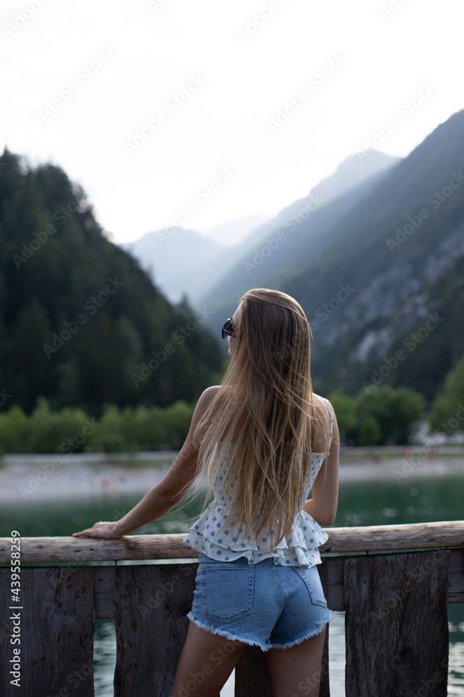 Woman standing on a bridge in the mountains. Young girl enjoying beauty of nature looking at mountain lake in Jezersko. Adventure travel in Slovenia, Europe. Woman standing on a bridge in the mountains. Young girl enjoying beauty of nature looking at mountain lake in Jezersko. Adventure travel in Slovenia, Europe.