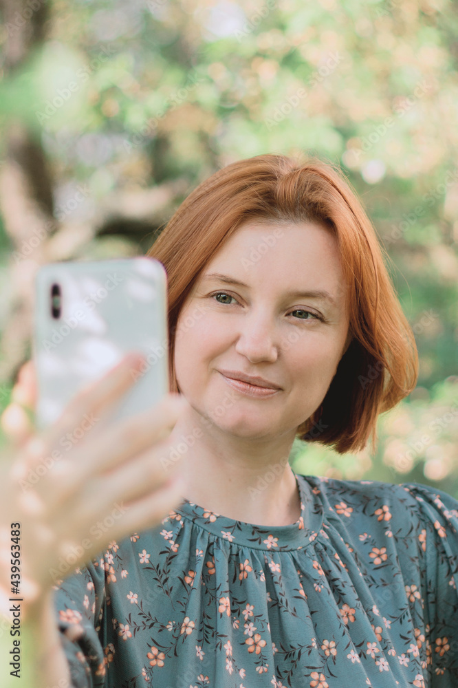 Close up portrait of red haired woman looking at screen of her smartphone, video chat communication, making selfie. Close up portrait of red haired woman looking at screen of her smartphone, video chat communication, making selfie.