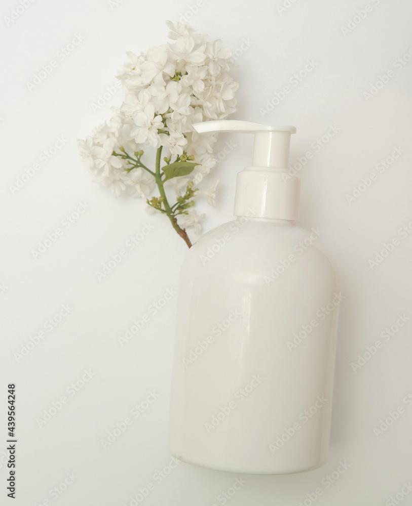 White bottle with a cosmetic product on a background with white lilac. White bottle with a cosmetic product on a background with white lilac.