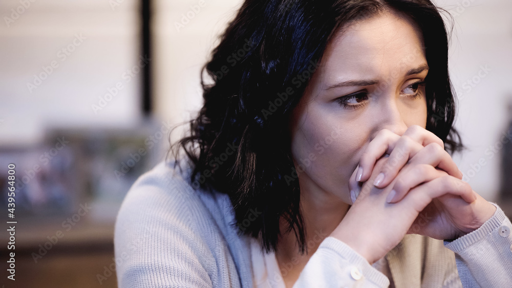 upset woman sitting and covering mouth with clenched hands at home upset woman sitting and covering mouth with clenched hands at home