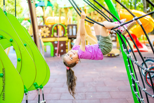 Little cheerful girl plays on vacation in the park at the playground. The child is having fun on the street on vacation. The child goes in for sports on simulators. 