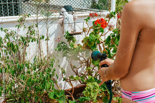 crop girl in swimwear watering plants with hosepipe