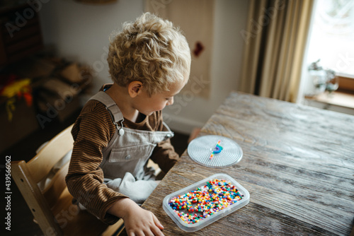 Blond boy playing with iron beads at a rustic wooden table