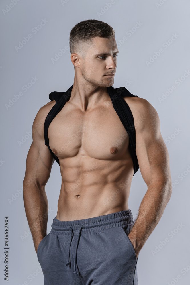 Young bodybuilder showing his muscular body against gray background Young bodybuilder showing his muscular body against gray background