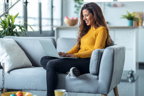 Pretty young woman working with her laptop while sitting on couch at home. Free Download Pretty young woman working with her laptop while sitting on couch at home. - GFXLoad