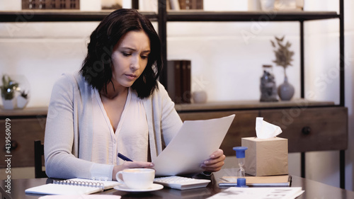 depressed woman sitting on table and looking through documents at home