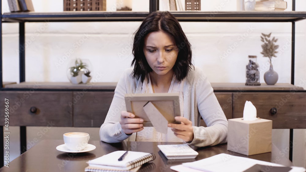 upset woman sitting on table and holding photo frame in hands at home upset woman sitting on table and holding photo frame in hands at home