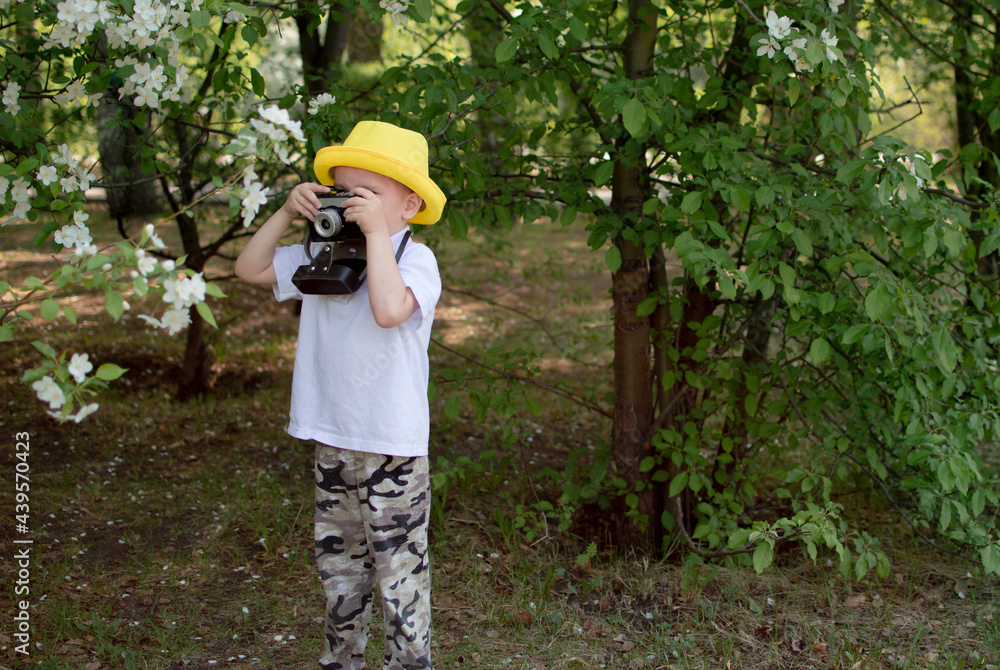 Child Taking Picture With Vintage Camera. Child in yellow summer hat holds camera in his hands, taking pictures of flowers in the park