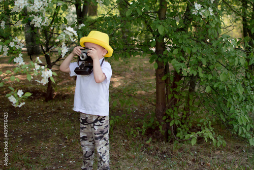 Child Taking Picture With Vintage Camera. Child in yellow summer hat holds camera in his hands, taking pictures of flowers in the park © Inna