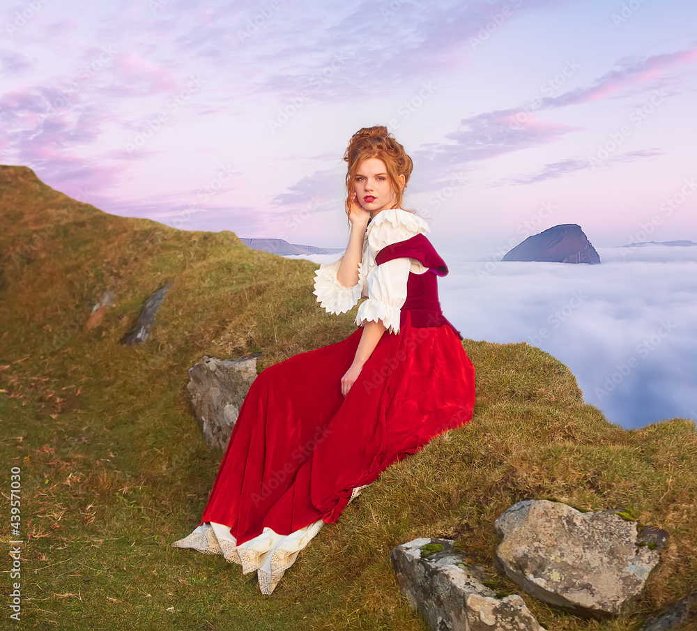 A redhead girl cosplayer sitting near Rock Witch's Finger. Vagar Island. Clouds covered the Atlantic Ocean. Faroe Islands