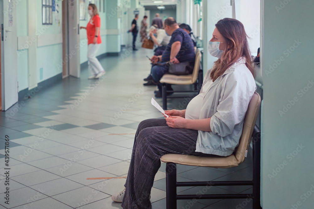 Pregnant woman in the corridor of the clinic with a medical mask on her face