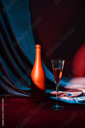 Wineglass and bottle of wine on a black reflective background. Red satin curtain flutters in the wind. photo
