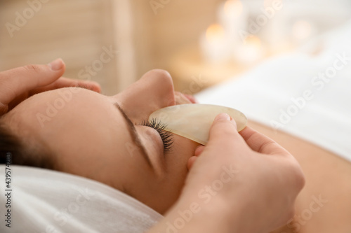 Young woman receiving facial massage with gua sha tool in beauty salon, closeup