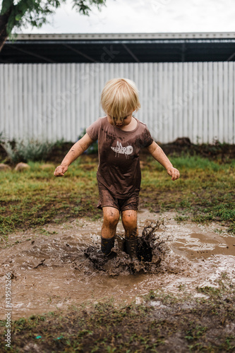 Female toddler splashing in mud puddle photo