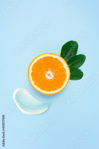 Fototapeta Naklejka Na Ścianę i Meble -  Creative beauty health fashion concept photo of orange slice with leaves and cream lotion swatches on blue background.