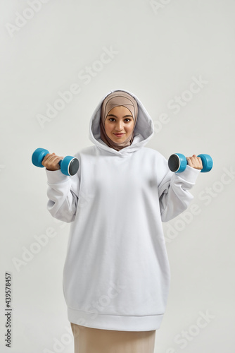 Happy young arabian girl in hijab lifting dumbbells
