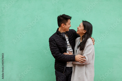 Happy Asian Couple Embrace in Front of a Mint Green Wall 