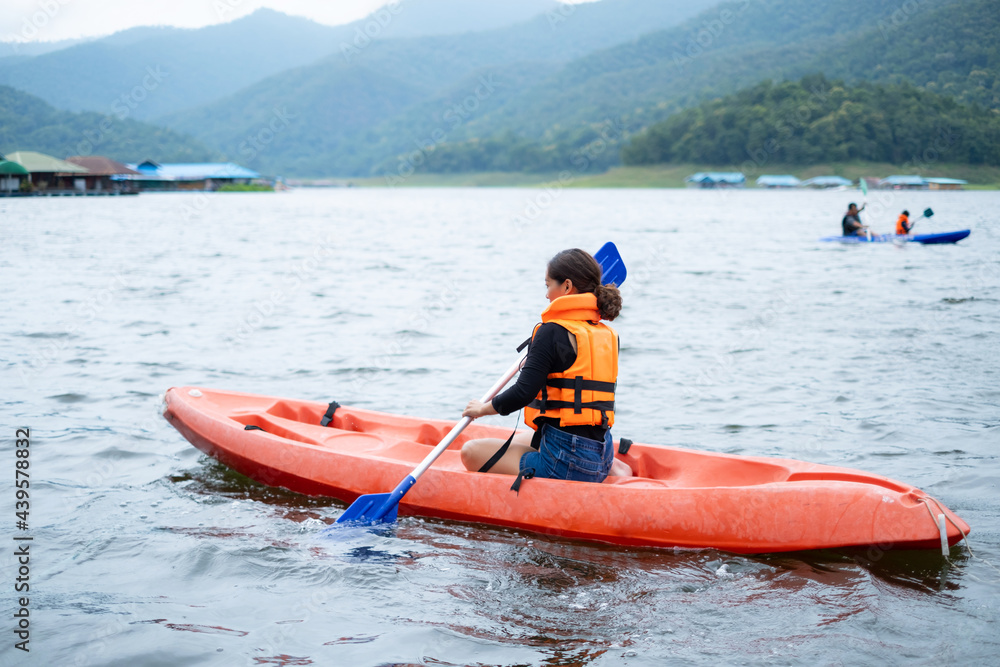 Asian girls in orange life jackets One person holds a paddle row the Kayak, against the backdrop of water and mountains Ready for travel as a hobby