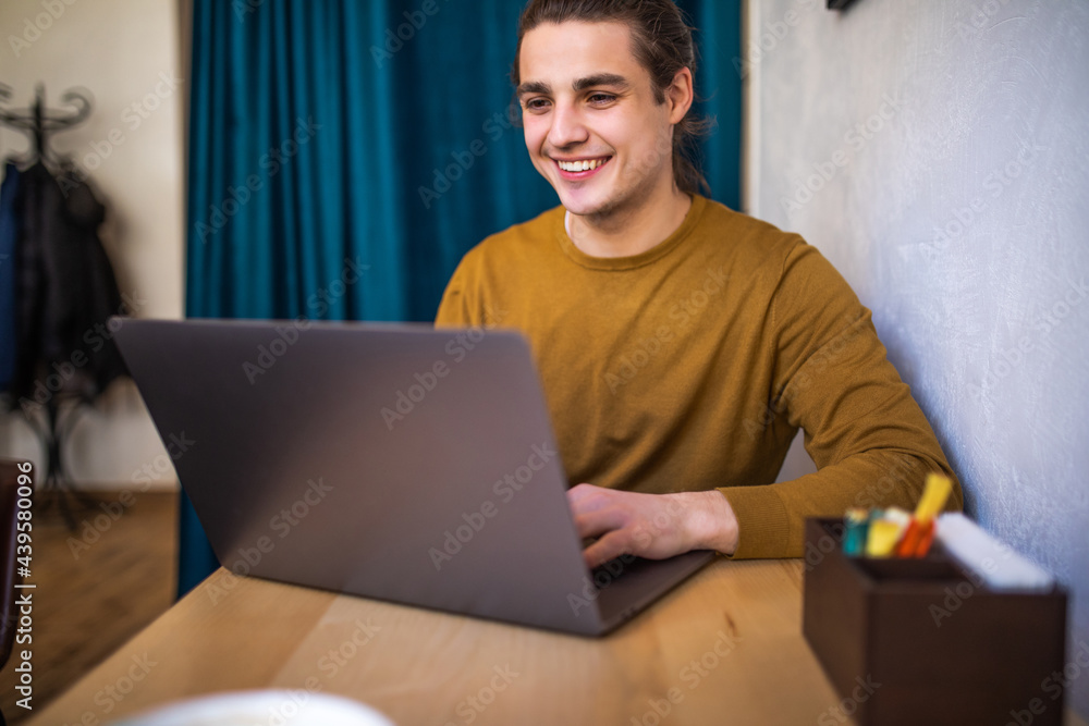 Handsome young man working on laptop and smiling while enjoying coffee in cafe Handsome young man working on laptop and smiling while enjoying coffee in cafe