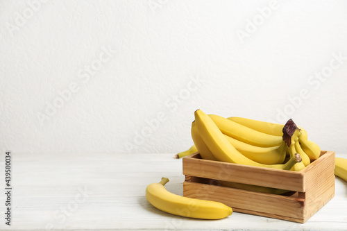 Ripe yellow bananas and crate on white wooden table. Space for text
