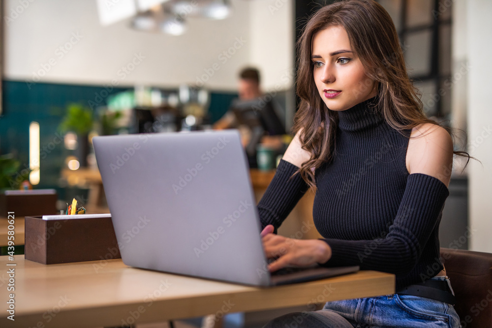 Beautiful young woman working on laptop and smiling while sitting in cafe Beautiful young woman working on laptop and smiling while sitting in cafe