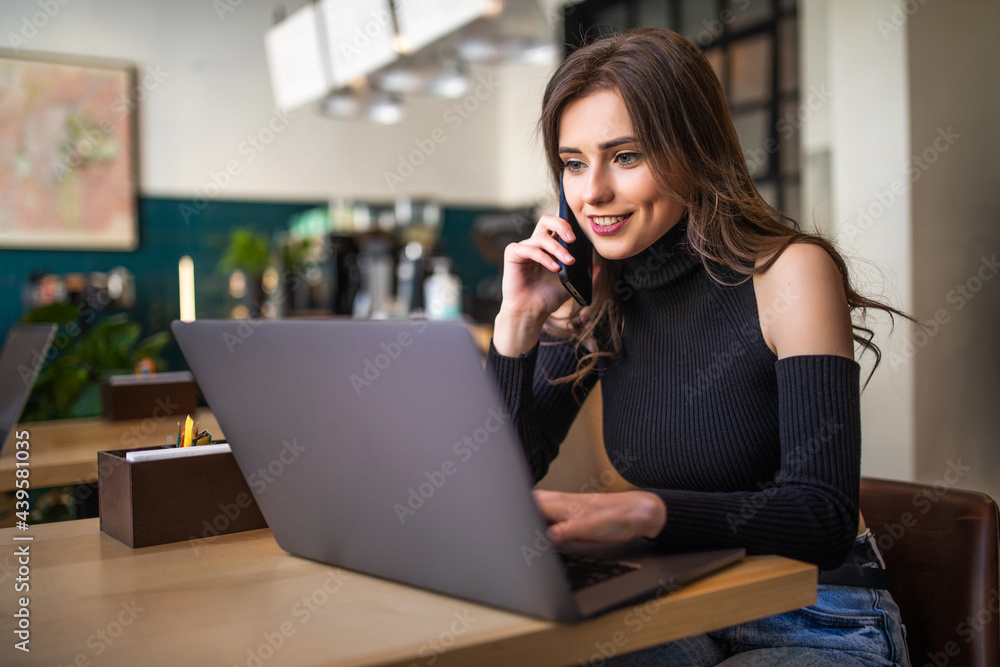 Happy young woman talking by mobile phone and using laptop at cafe Happy young woman talking by mobile phone and using laptop at cafe