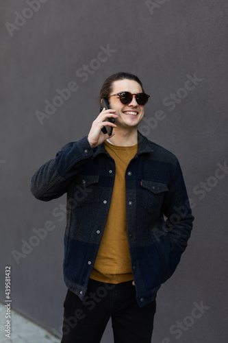 Full body side portrait of a smiling young man walking on sidewalk and listening to mobile phone